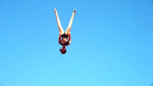 An inflatable sex doll is in the air, upside down, against a bright blue sky